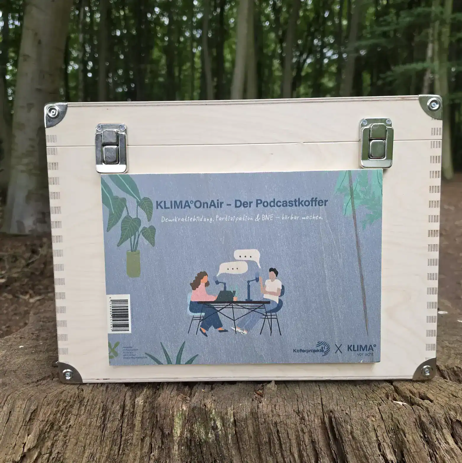Der KLIMA°OnAir Podcastkoffer von Kofferprojekte21 und KLIMA° vor acht – Holzkoffer mit dem Podcastkoffer-Deckel im Wald
