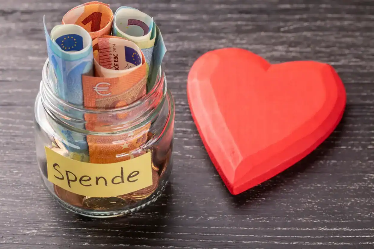 Ein Glas mit Euro-Scheinen und Münzen, versehen mit einem Zettel „Spende“, daneben ein rotes Holzherz